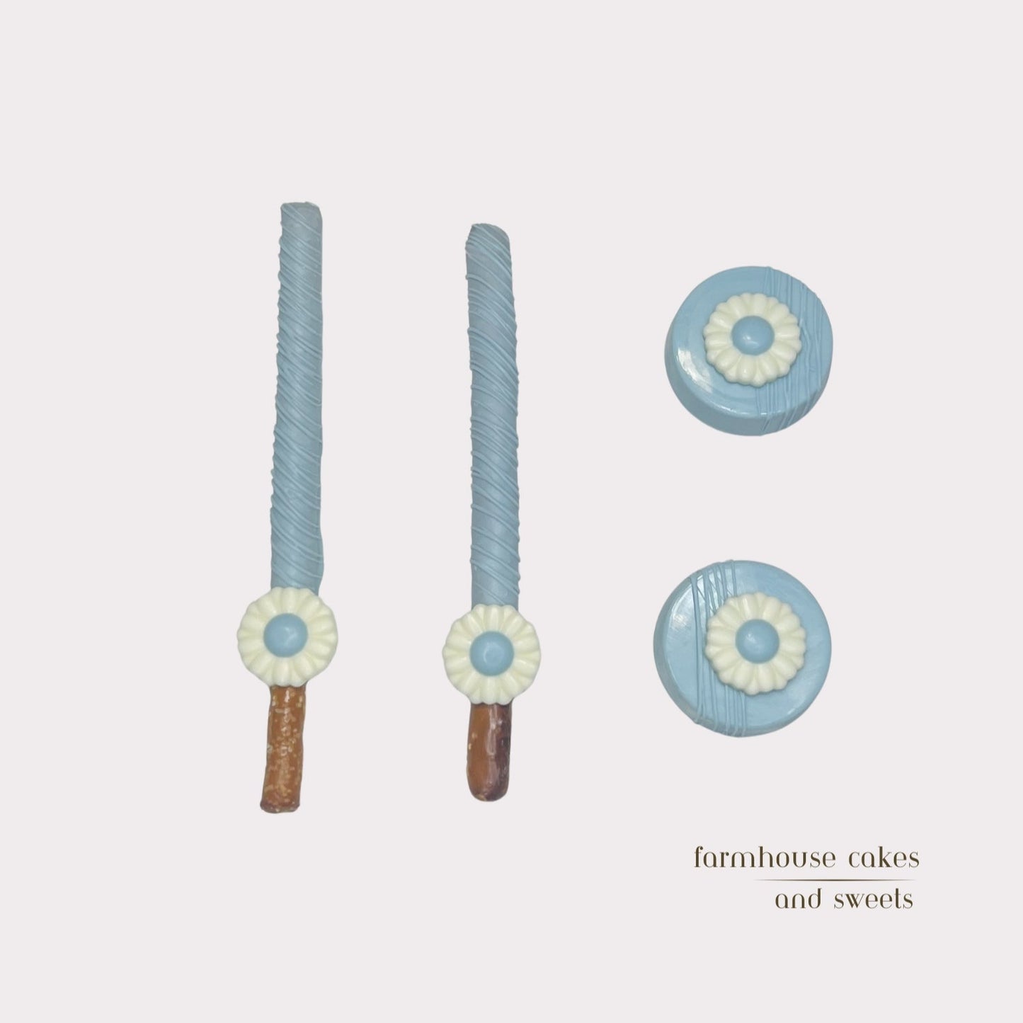 Soft pastel blue chocolate-covered Oreos and pretzel rods topped with drizzle and white chocolate daisies, handcrafted by Farmhouse Cakes and Sweets for Spring gifts and celebrations.