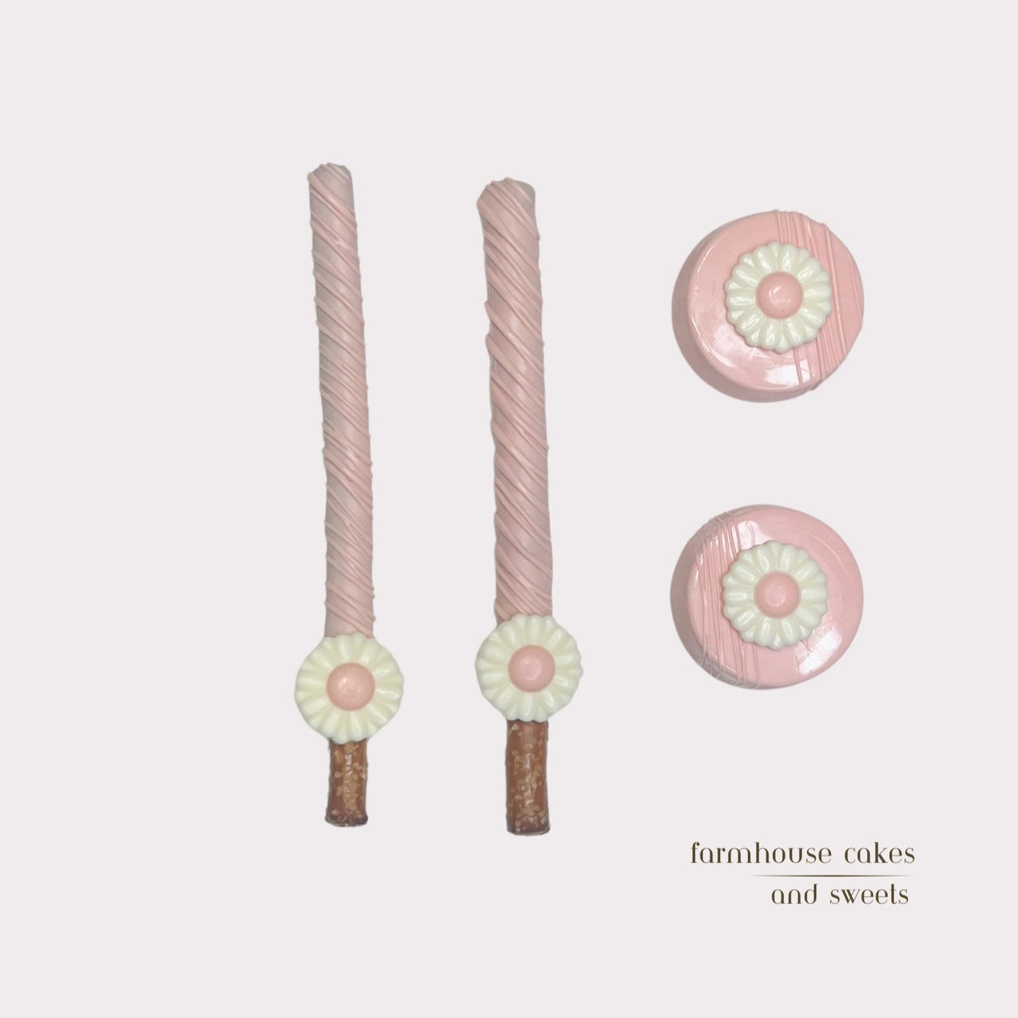 Soft pastel pink chocolate-covered Oreos and pretzel rods topped with drizzle and white chocolate daisies, handcrafted by Farmhouse Cakes and Sweets for Spring gifts and celebrations
