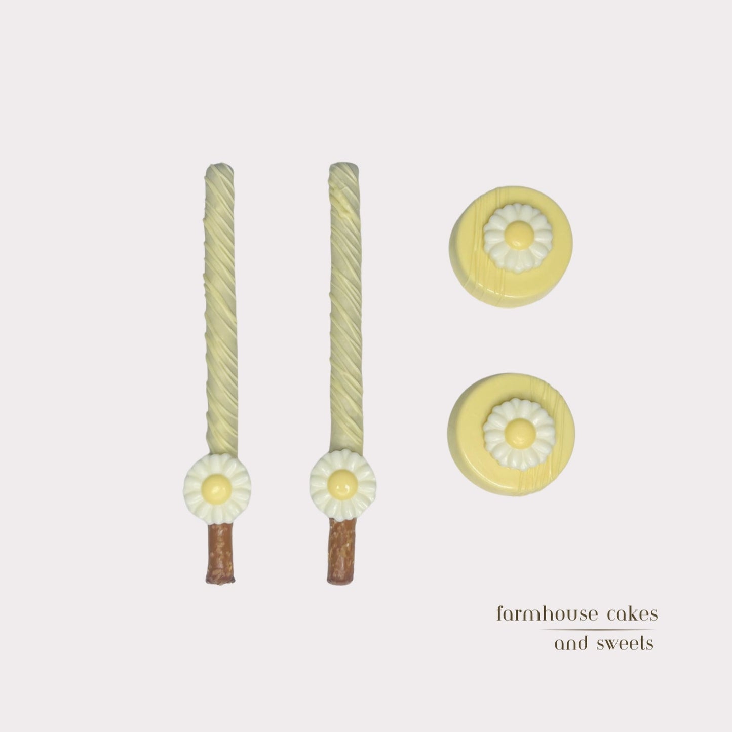 Soft pastel yellow chocolate-covered Oreos and pretzel rods topped with drizzle and white chocolate daisies, handcrafted by Farmhouse Cakes and Sweets for Spring gifts and celebrations.