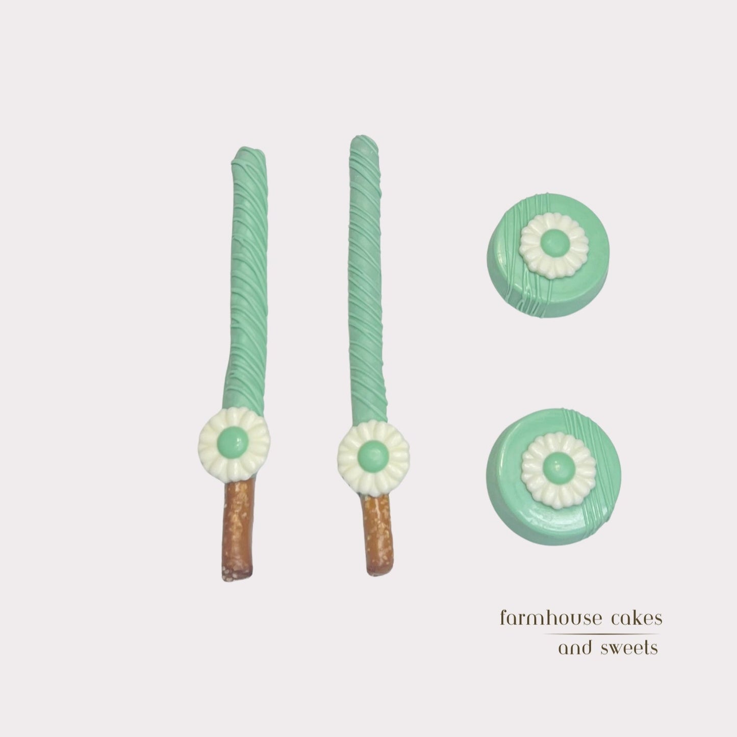 Soft pastel green chocolate-covered Oreos and pretzel rods topped with drizzle and white chocolate daisies, handcrafted by Farmhouse Cakes and Sweets for Spring gifts and celebrations.