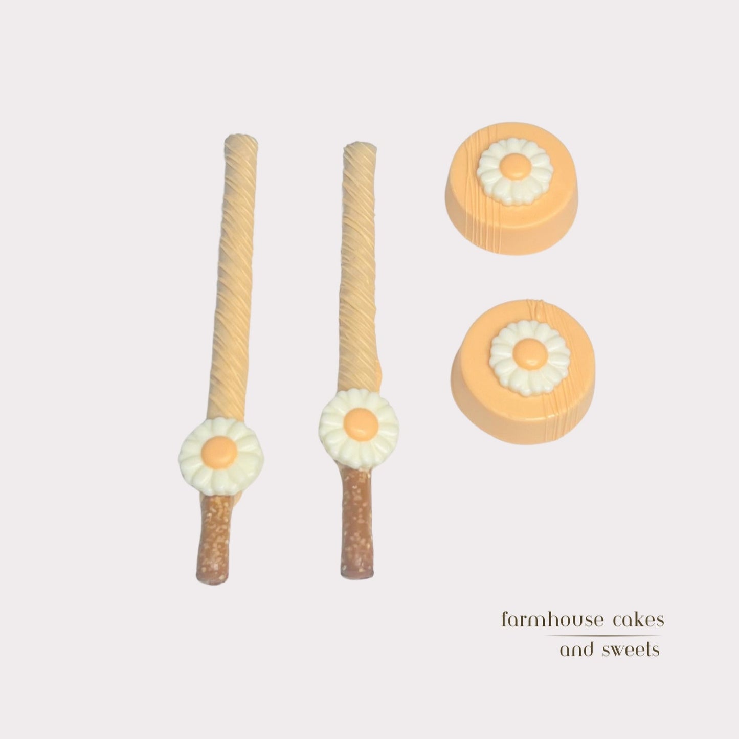 Soft pastel orange chocolate-covered Oreos and pretzel rods topped with drizzle and white chocolate daisies, handcrafted by Farmhouse Cakes and Sweets for Spring gifts and celebrations.
