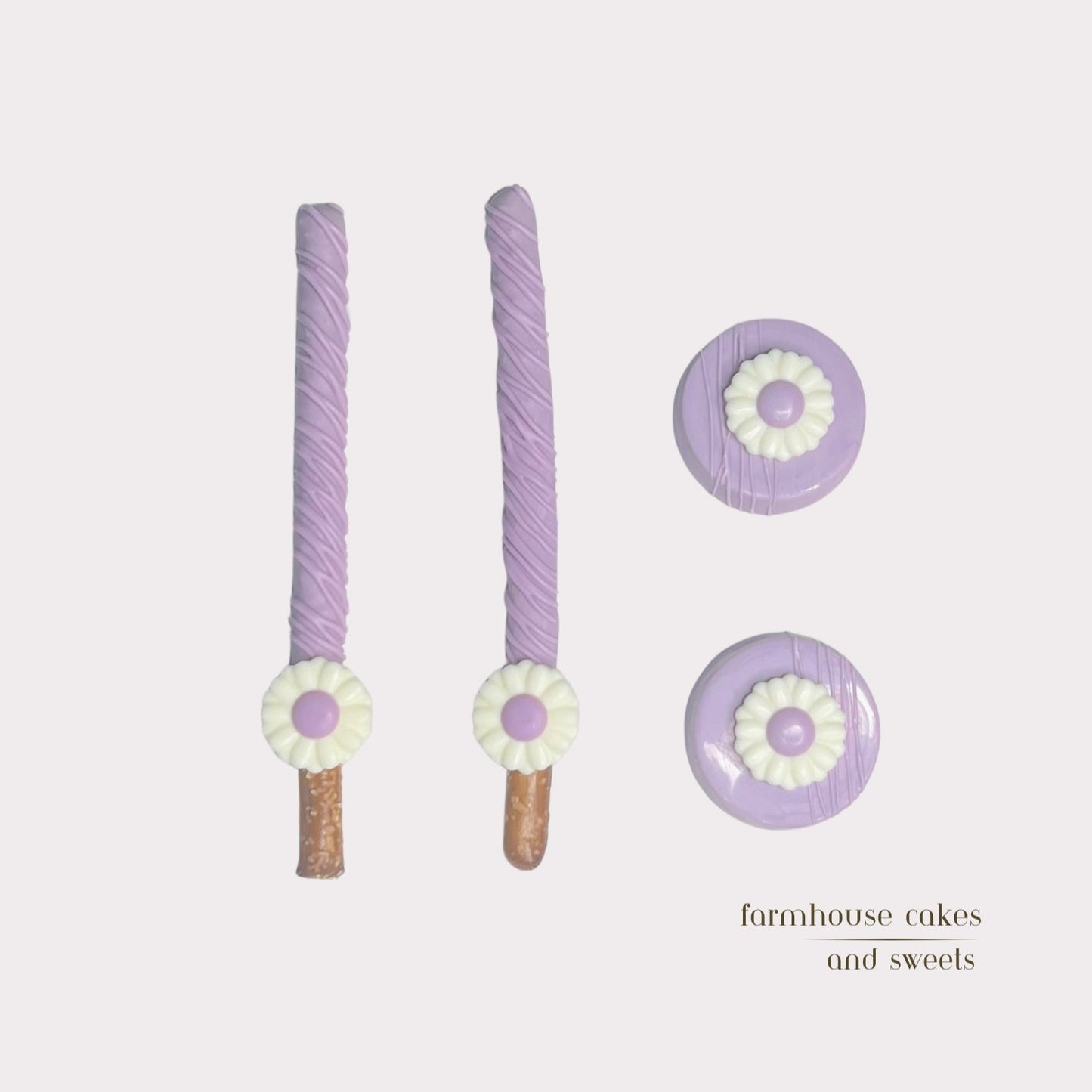 Soft pastel purple chocolate-covered Oreos and pretzel rods topped with drizzle and white chocolate daisies, handcrafted by Farmhouse Cakes and Sweets for Spring gifts and celebrations.