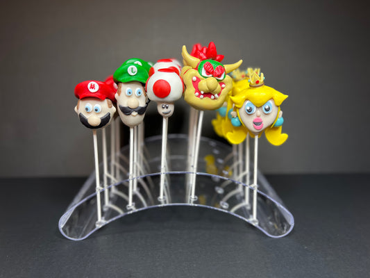 Handcrafted character cake pops inspired by classic red-cap, green-cap, and mushroom heroes, made by Farmhouse Cakes and Sweets for a custom party order.