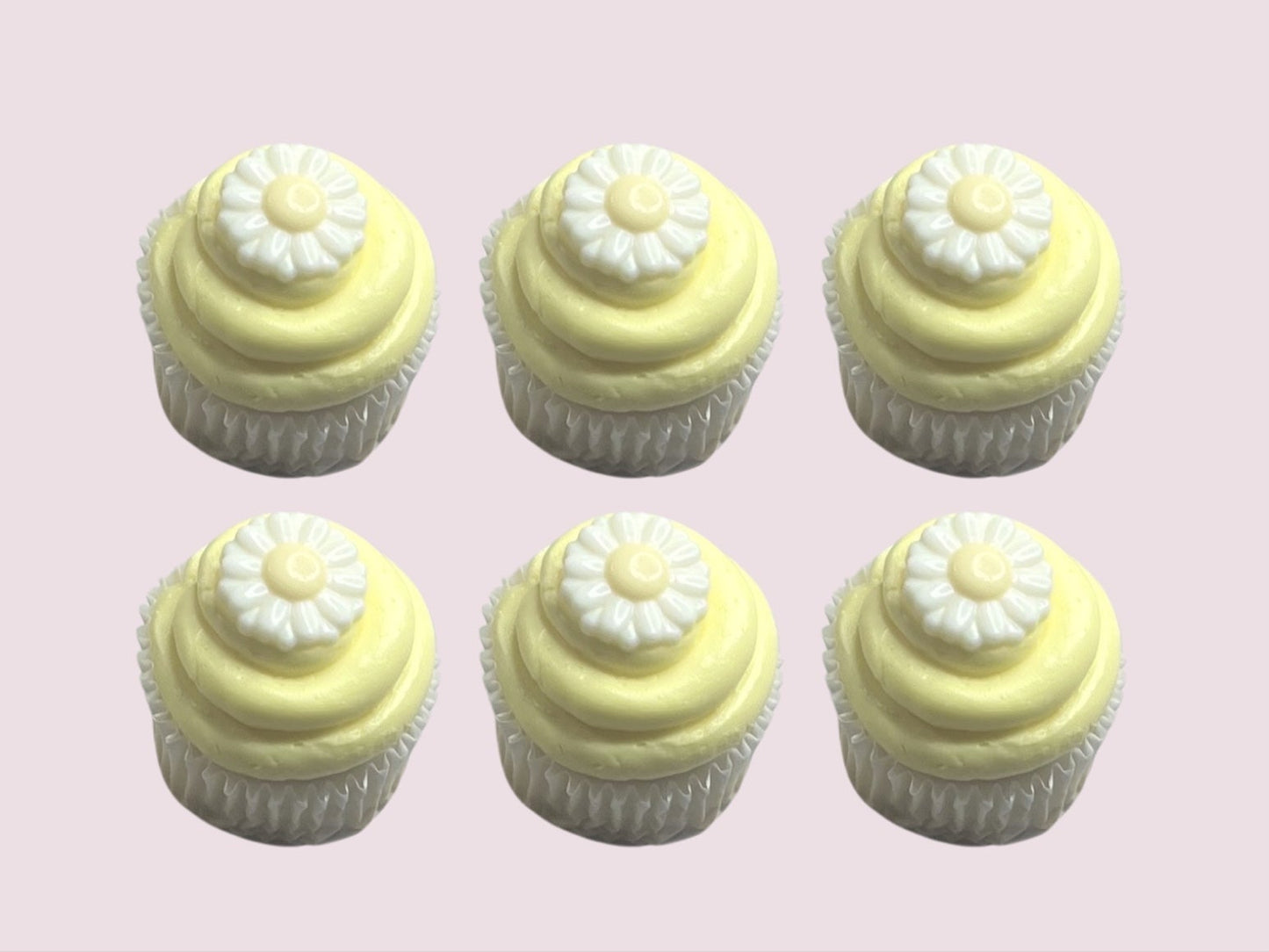 Set of six pastel yellow frosted cupcakes topped with white chocolate daisy decorations, ideal for spring events and gifting.