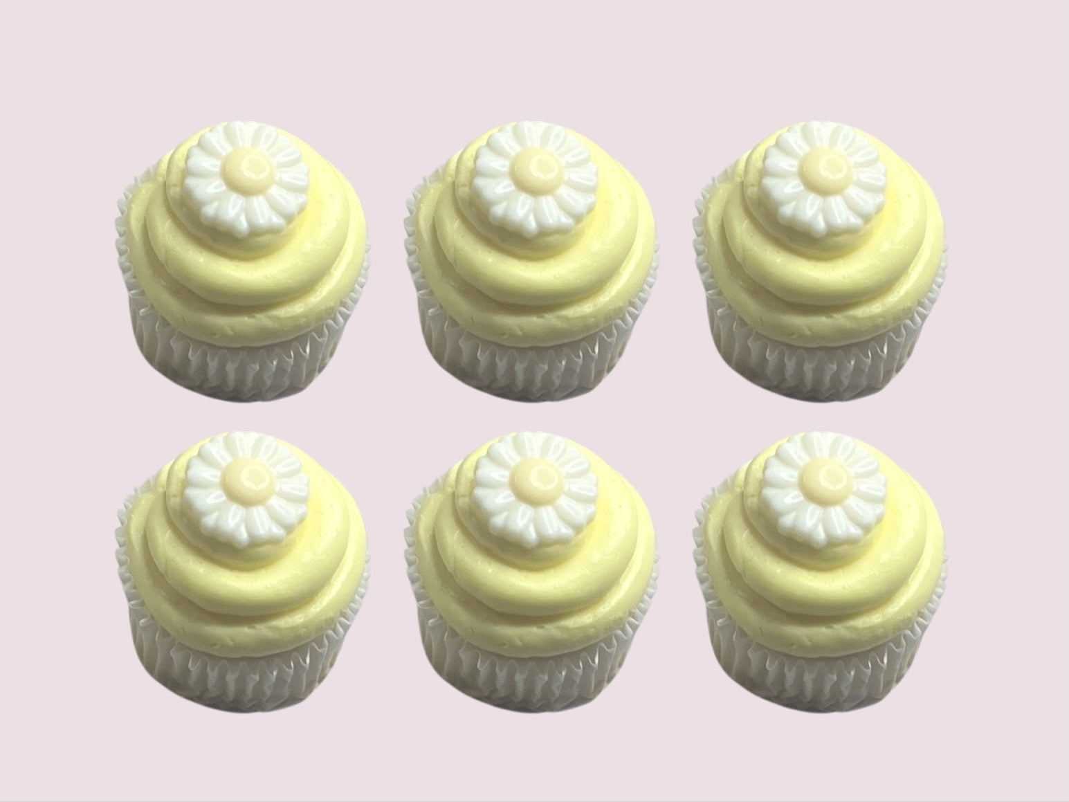 Set of six pastel yellow frosted cupcakes topped with white chocolate daisy decorations, ideal for spring events and gifting.